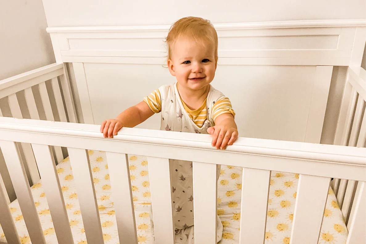 A 10-month-old baby standing while holding the crib rail in a dimly lit bedroom at night, realistic family photograph