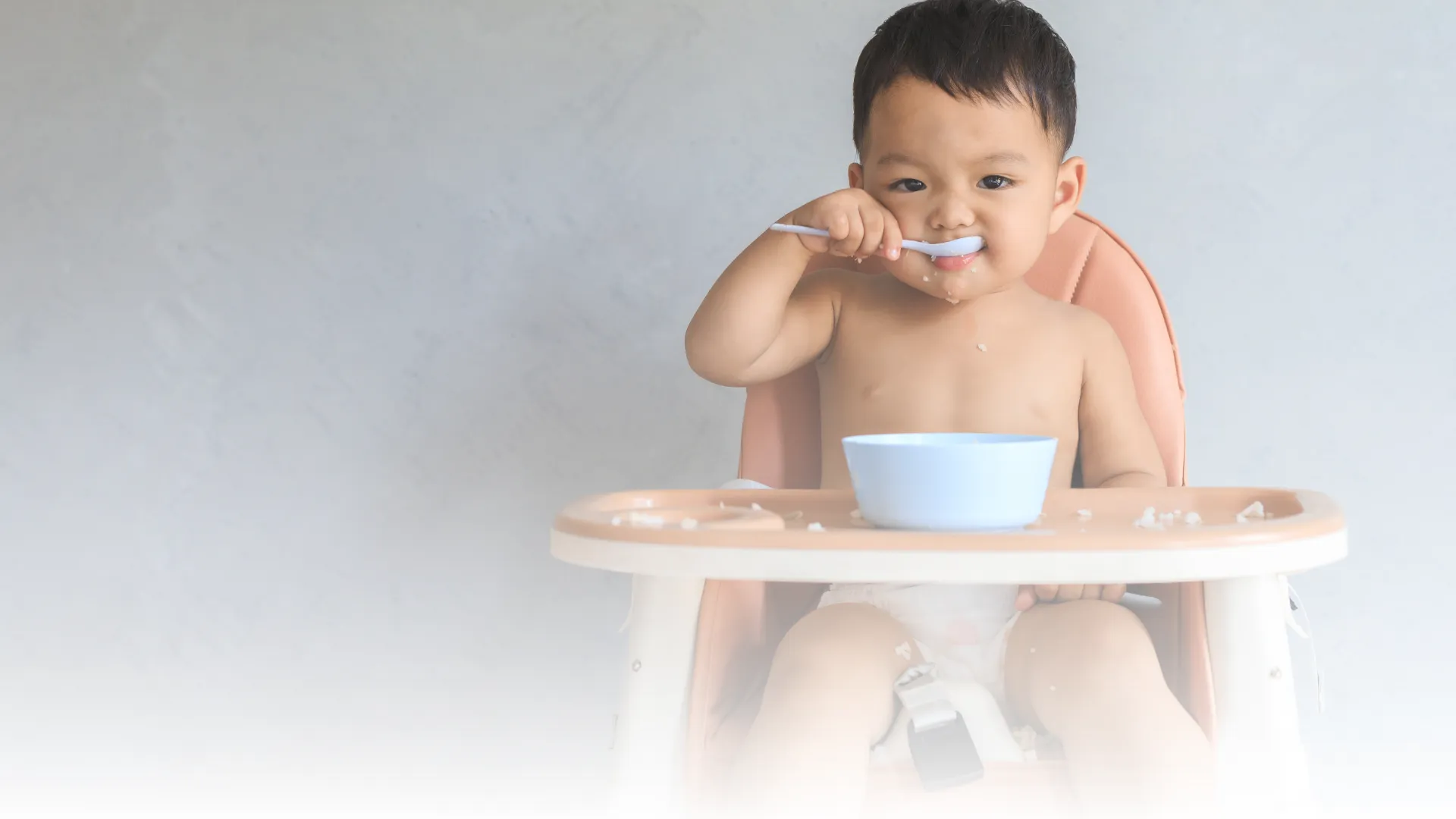 A baby sitting in a high chair with visible hives on the cheeks and chin, looking uncomfortable while a caregiver watches closely, realistic indoor photo