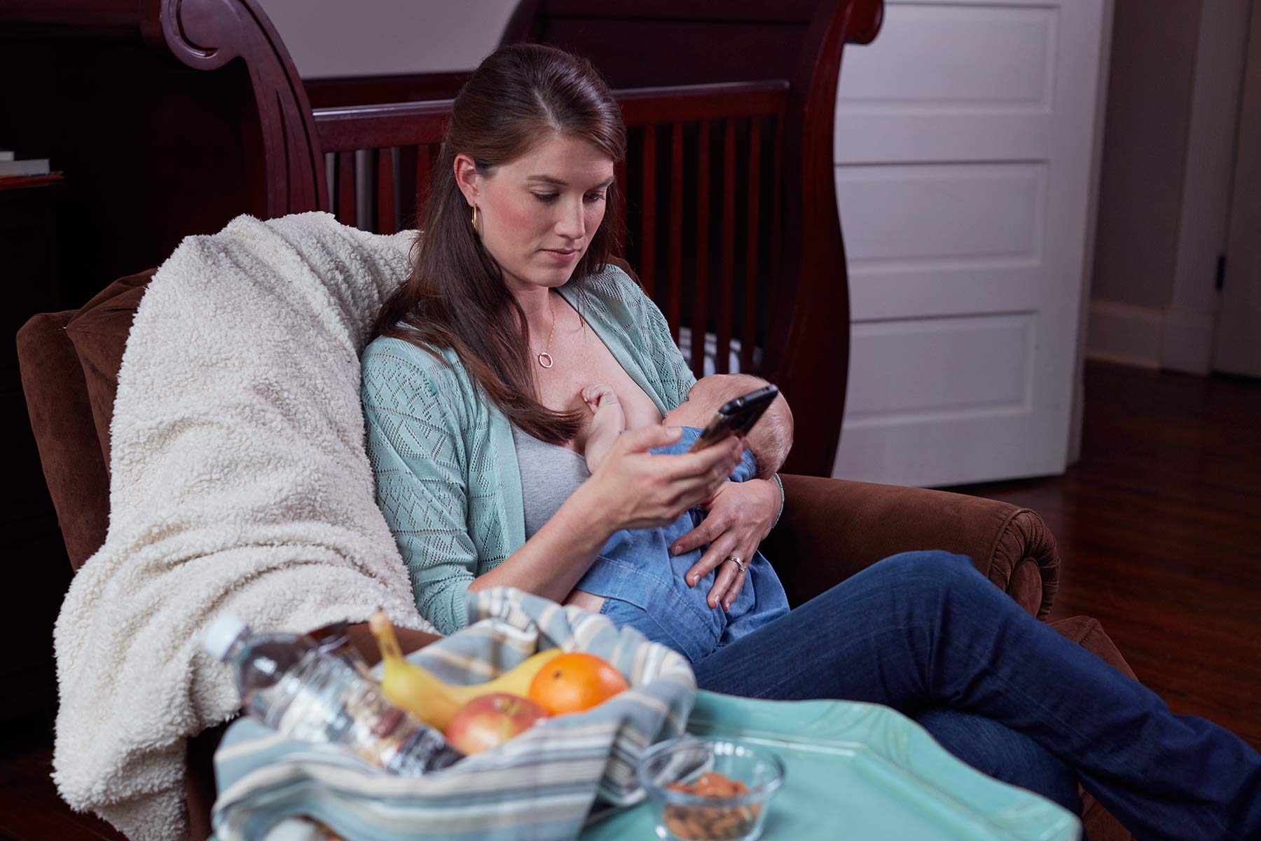 A breastfed baby turning their head to look around while latched, parent seated on a couch in a bright living room