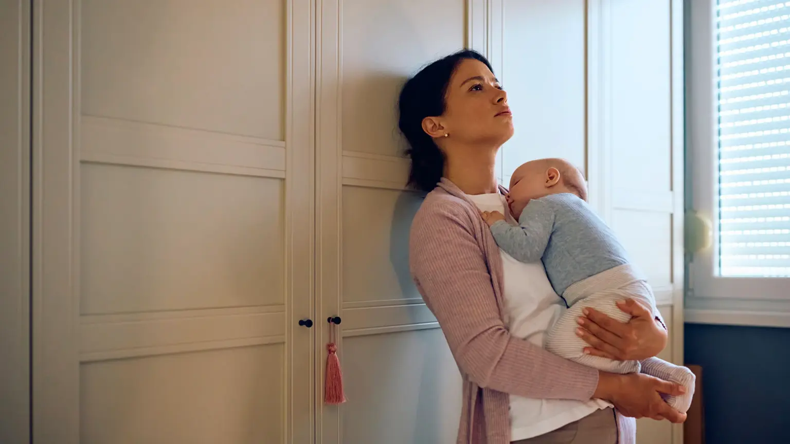 A calm parent holding a sleeping infant near a sunlit window at home, realistic lifestyle photo