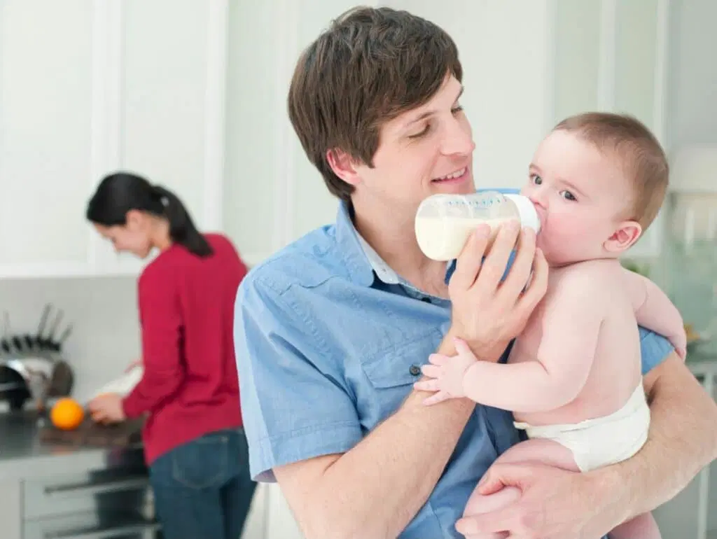 A caregiver holding a baby in a semi-upright position and offering a bottle held nearly horizontal to slow milk flow, real photograph