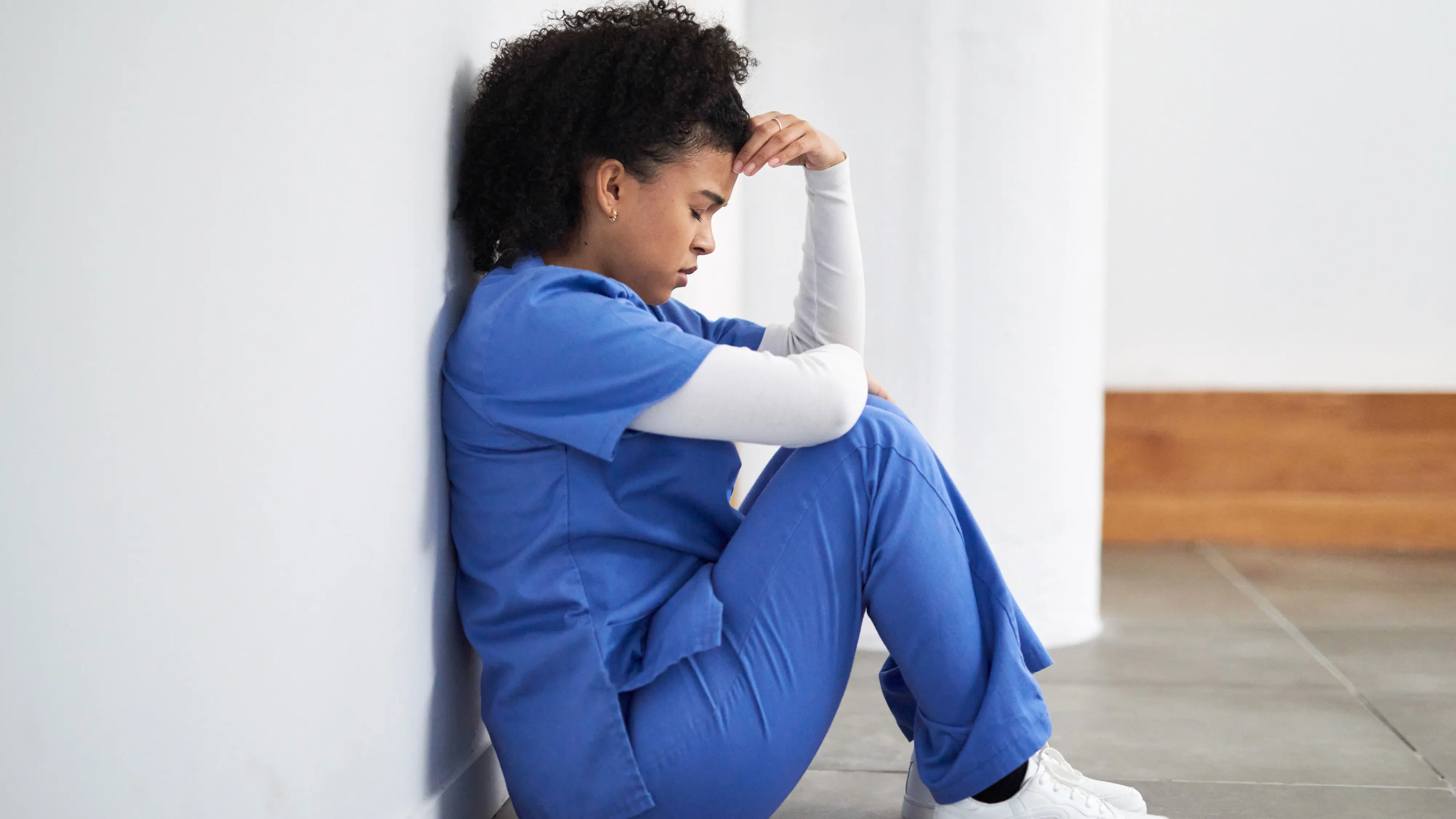 A child in casual clothes standing in a hallway holding their stomach near a bathroom door, showing mild discomfort, natural indoor lighting