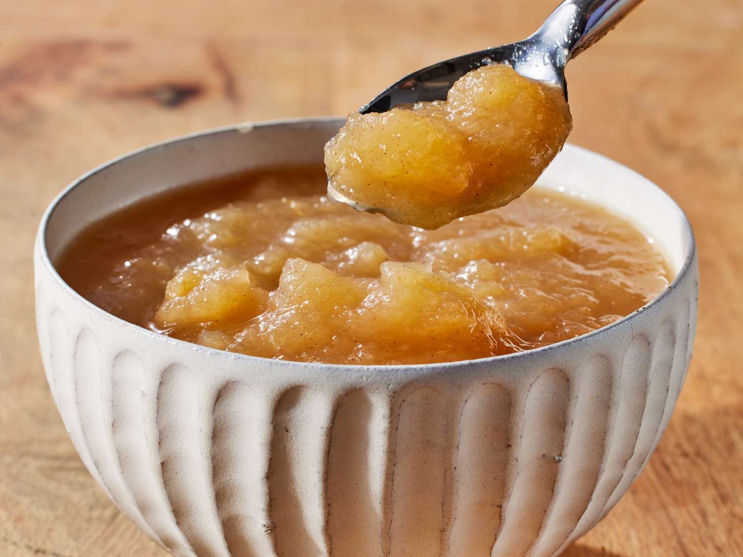 A close-up photo of a small spoon holding a spoonful of applesauce over a kitchen counter, natural light, shallow depth of field