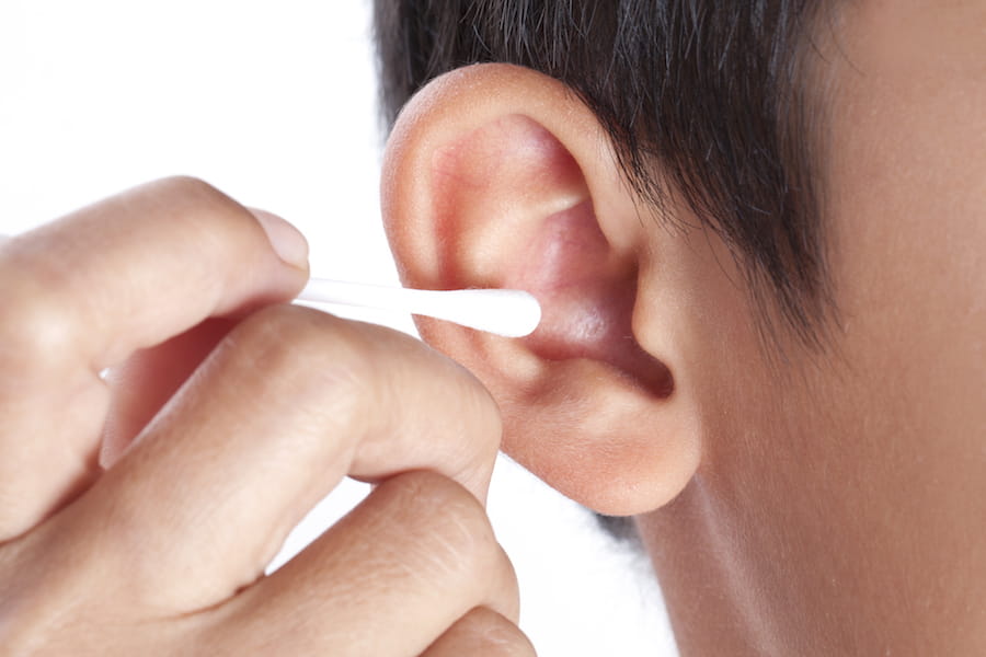 A close-up photo of an adult hand holding a cotton swab next to a toddler's ear without inserting it, cautionary real-life scene