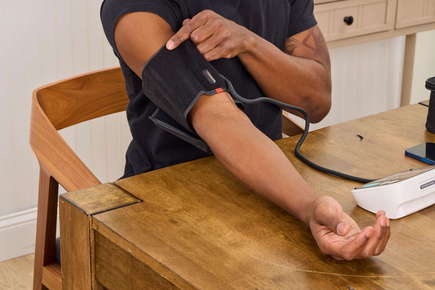 A close-up photo of an automatic upper arm blood pressure cuff wrapped around an adult arm in a home setting, realistic photo