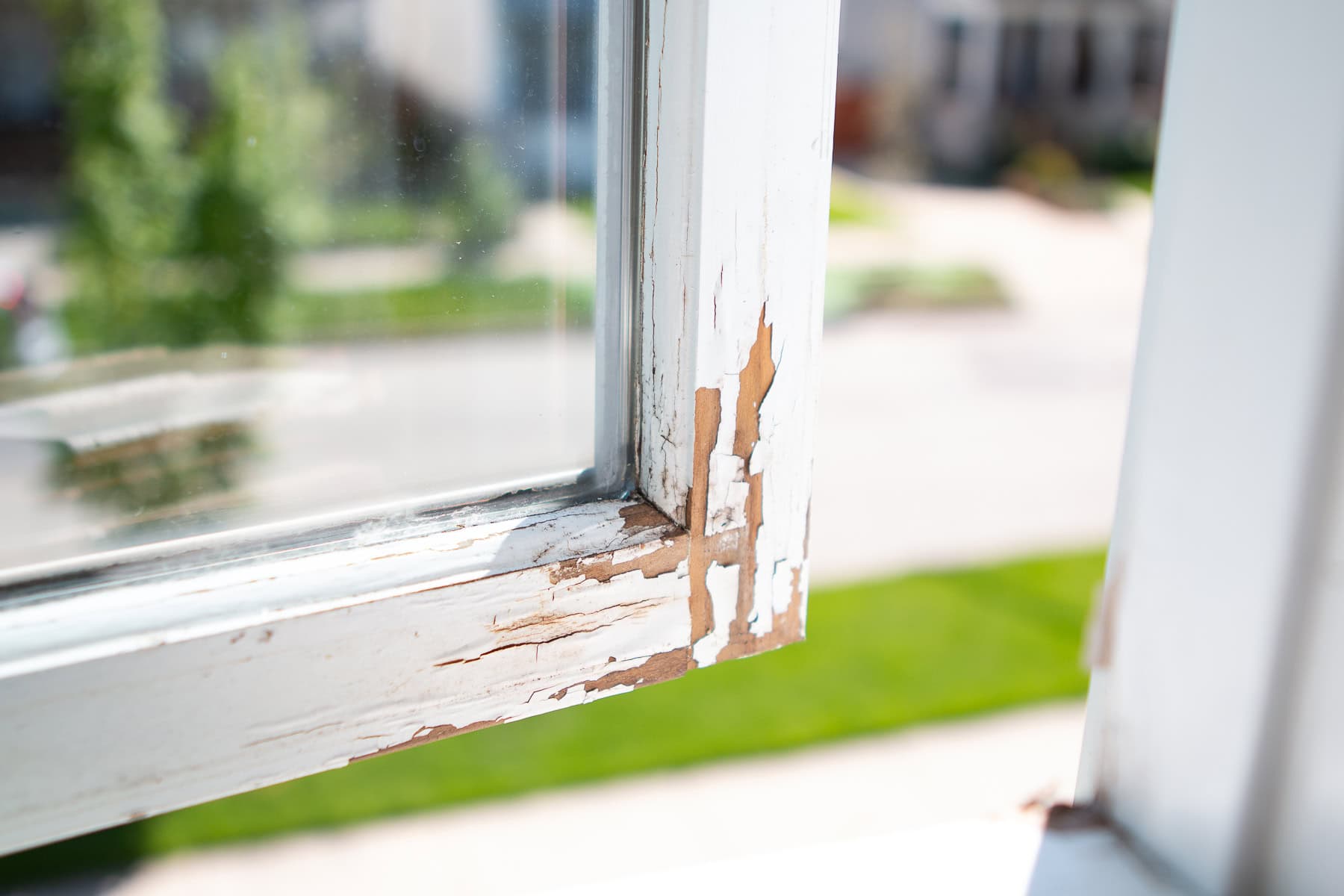 A close-up photo of an older home window frame with peeling paint and visible dust in the window well, realistic lighting