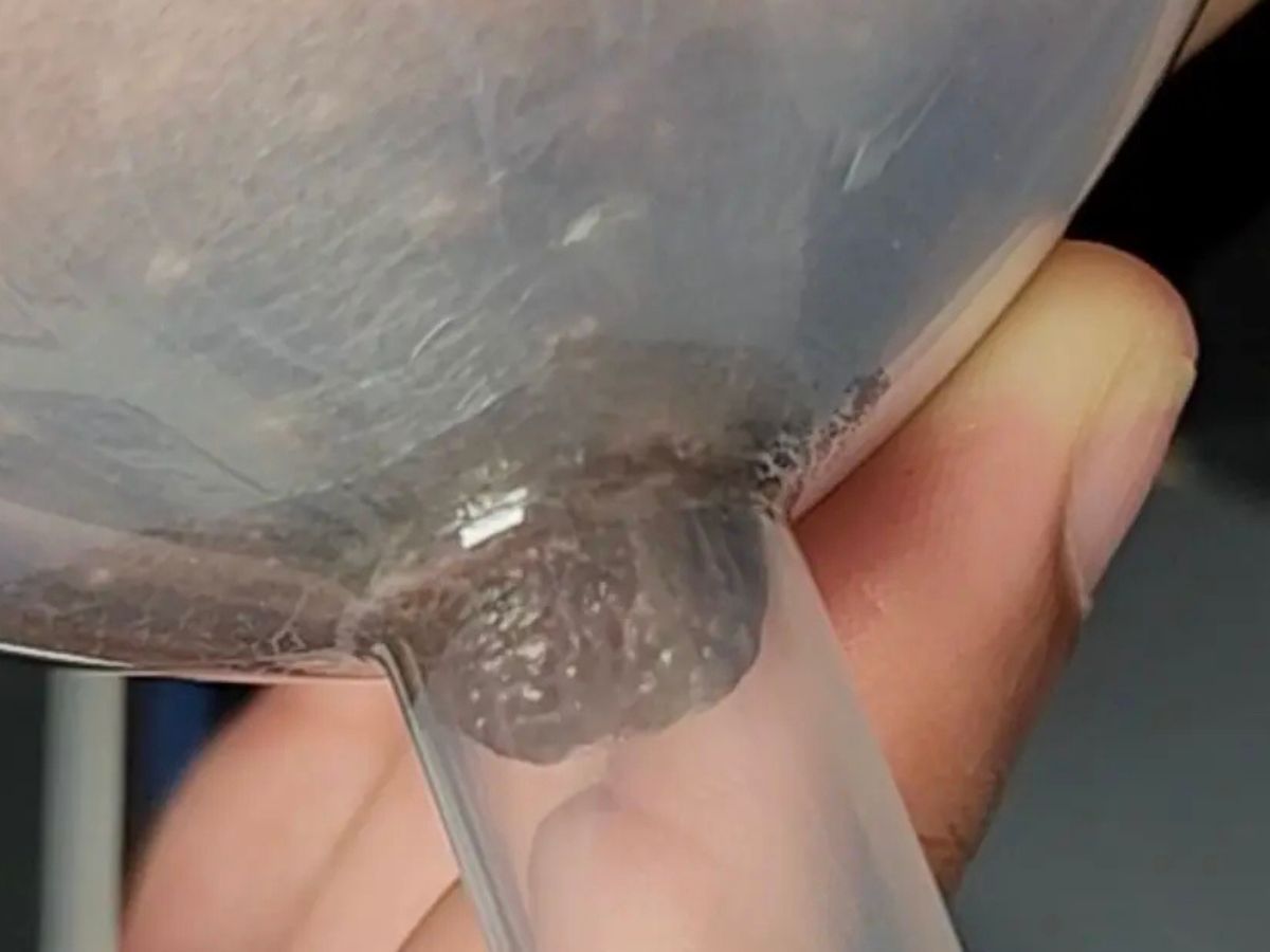 A close-up photo of hands holding a breast pump flange near a pumping bra, showing careful fitting and alignment of the nipple in the flange tunnel