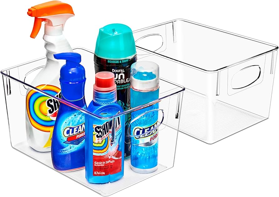 A curious toddler sitting on a kitchen floor near a closed under-sink cabinet, with cleaning supplies stored up high on a counter in the background, real-life home photo