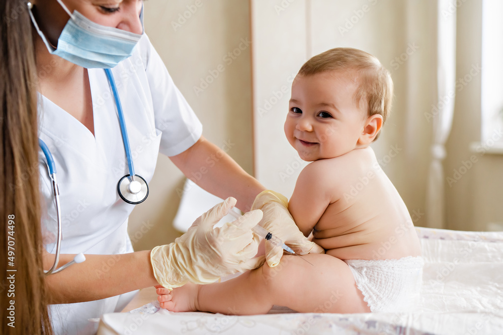 A hospital nurse wearing gloves administering a small injection into a newborn’s outer thigh while the baby is swaddled, realistic clinical photo