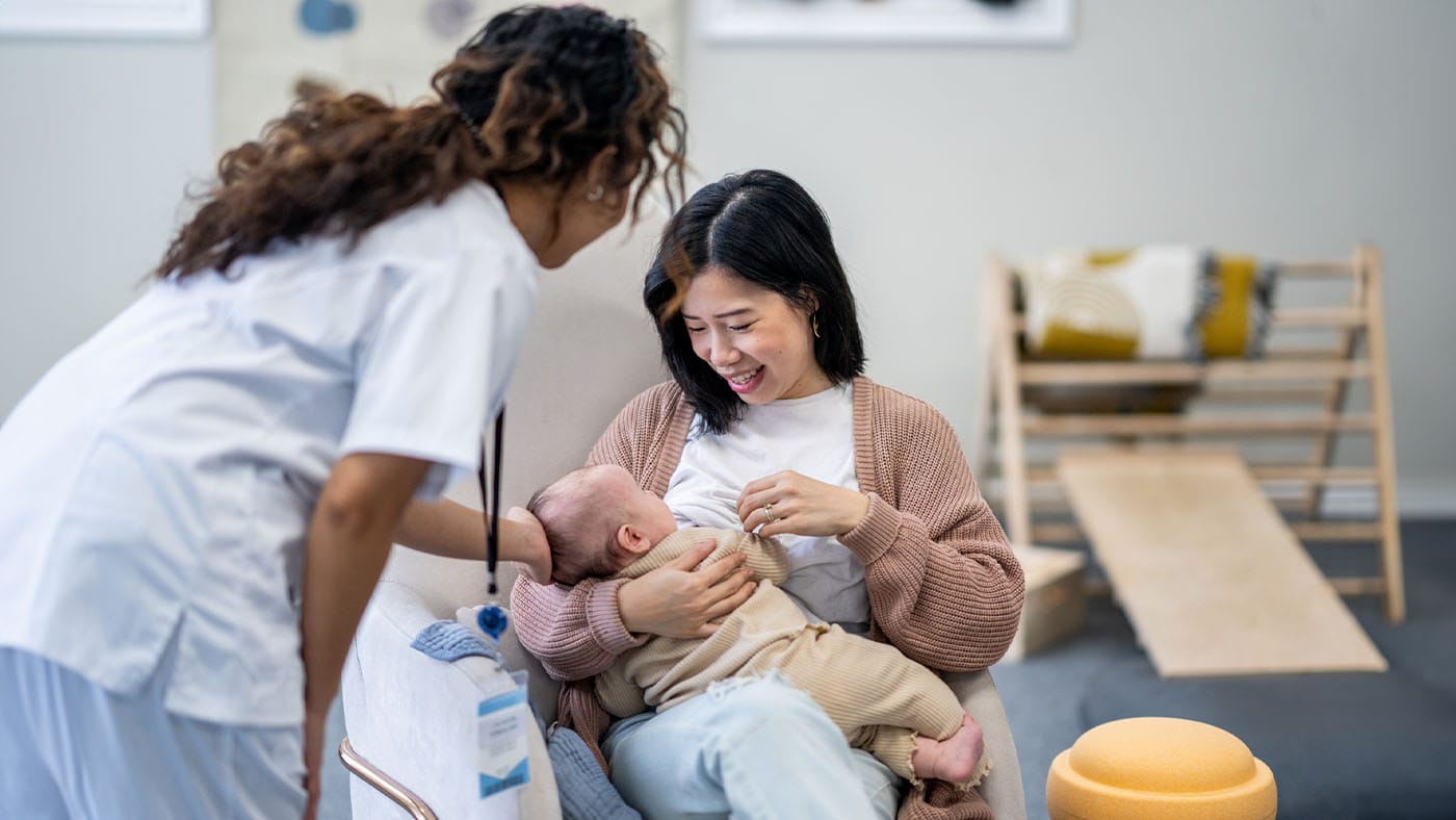 A lactation consultant sitting beside a breastfeeding parent in a clinic room, gently guiding the baby into a deeper latch, realistic photography