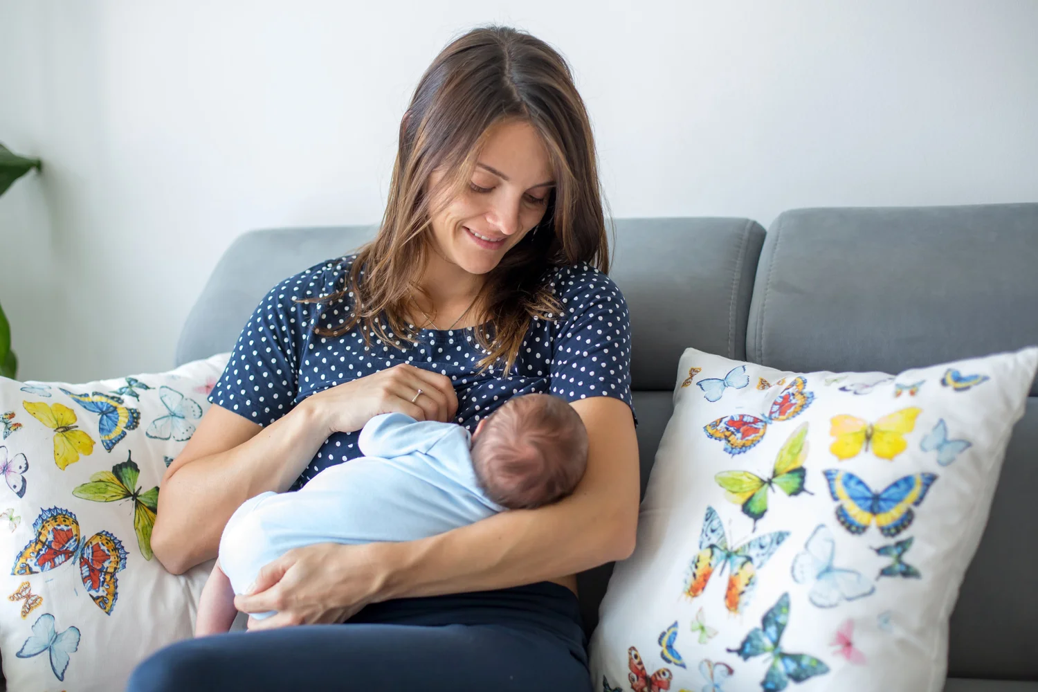 A lactation consultant sitting beside a parent on a couch during a calm home visit, observing a newborn feeding and offering supportive guidance, realistic photography