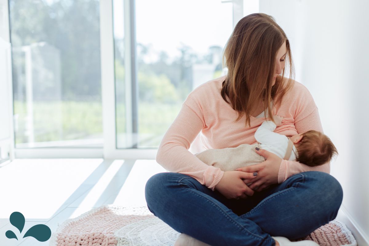 A mother breastfeeding her baby in a chair near a window with soft morning light, peaceful home photo