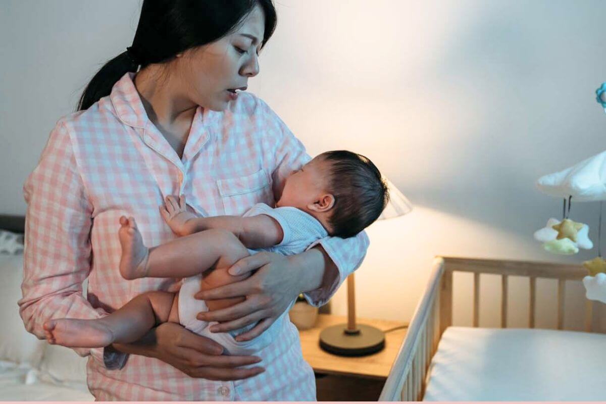 A mother gently rocking a 3-month-old baby in a dim nursery beside a crib, realistic home photo