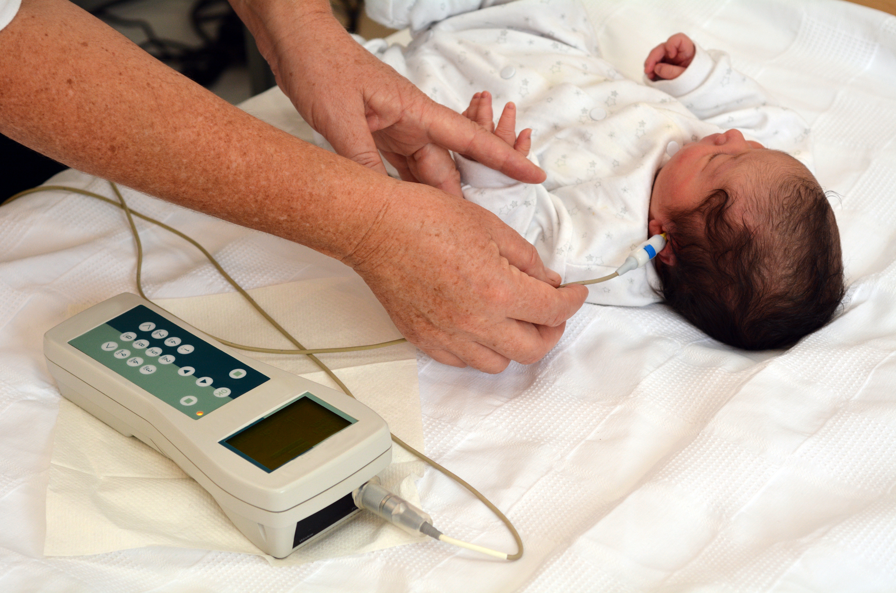 A newborn baby in a hospital bassinet while a nurse performs a hearing screen with small sensors, candid hospital photography style
