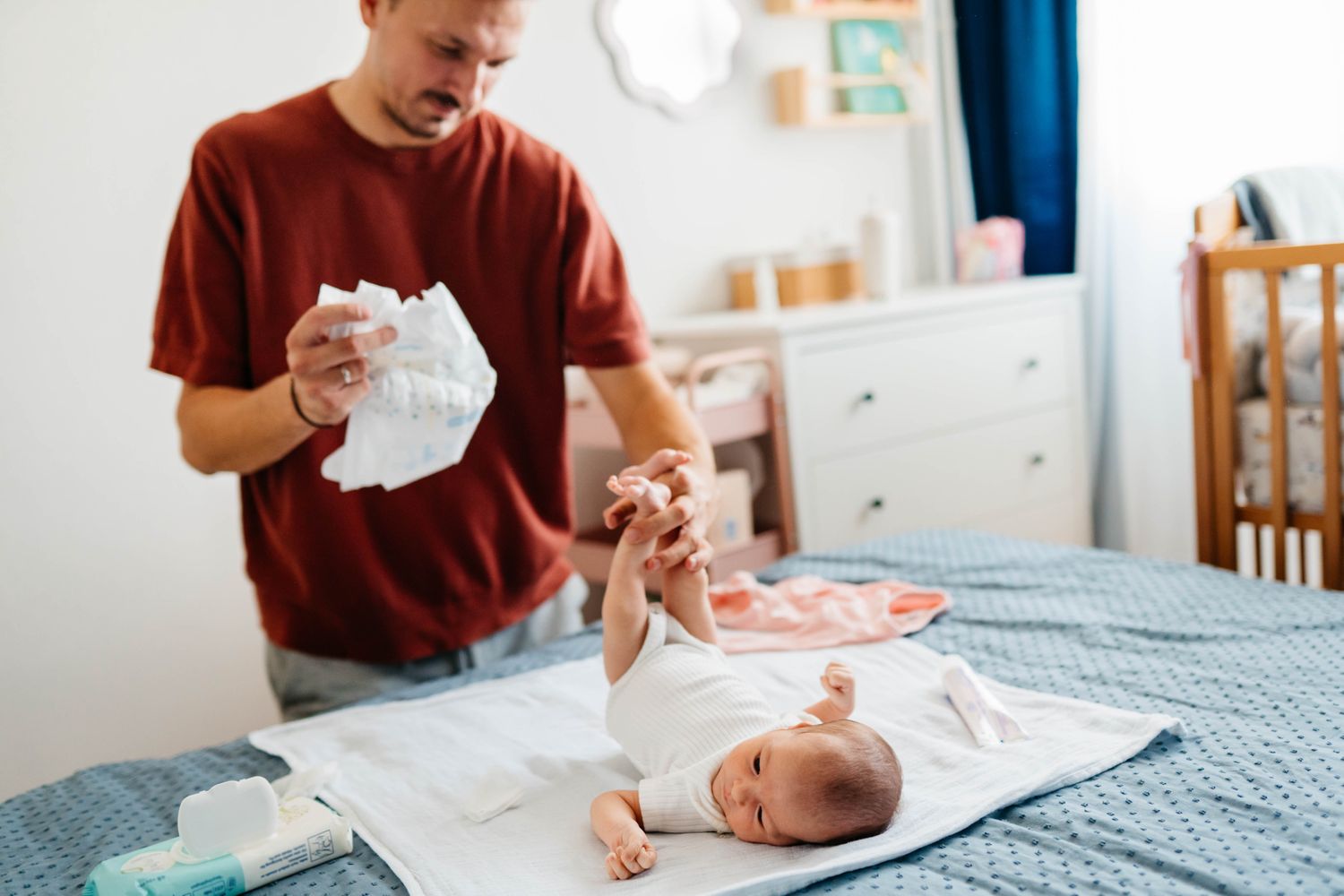 A newborn baby lying on a changing pad while a parent gently checks the diaper in a softly lit bedroom, real-life candid photo