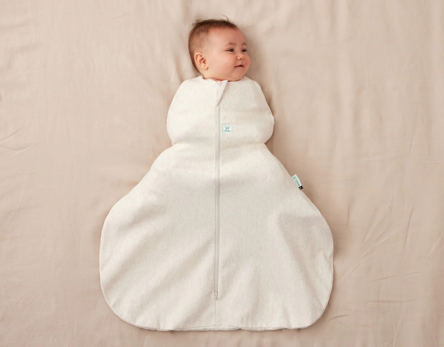 A newborn lying on a bed in a swaddle that is snug around the torso and loose around the hips and legs, with knees bent comfortably, realistic photo