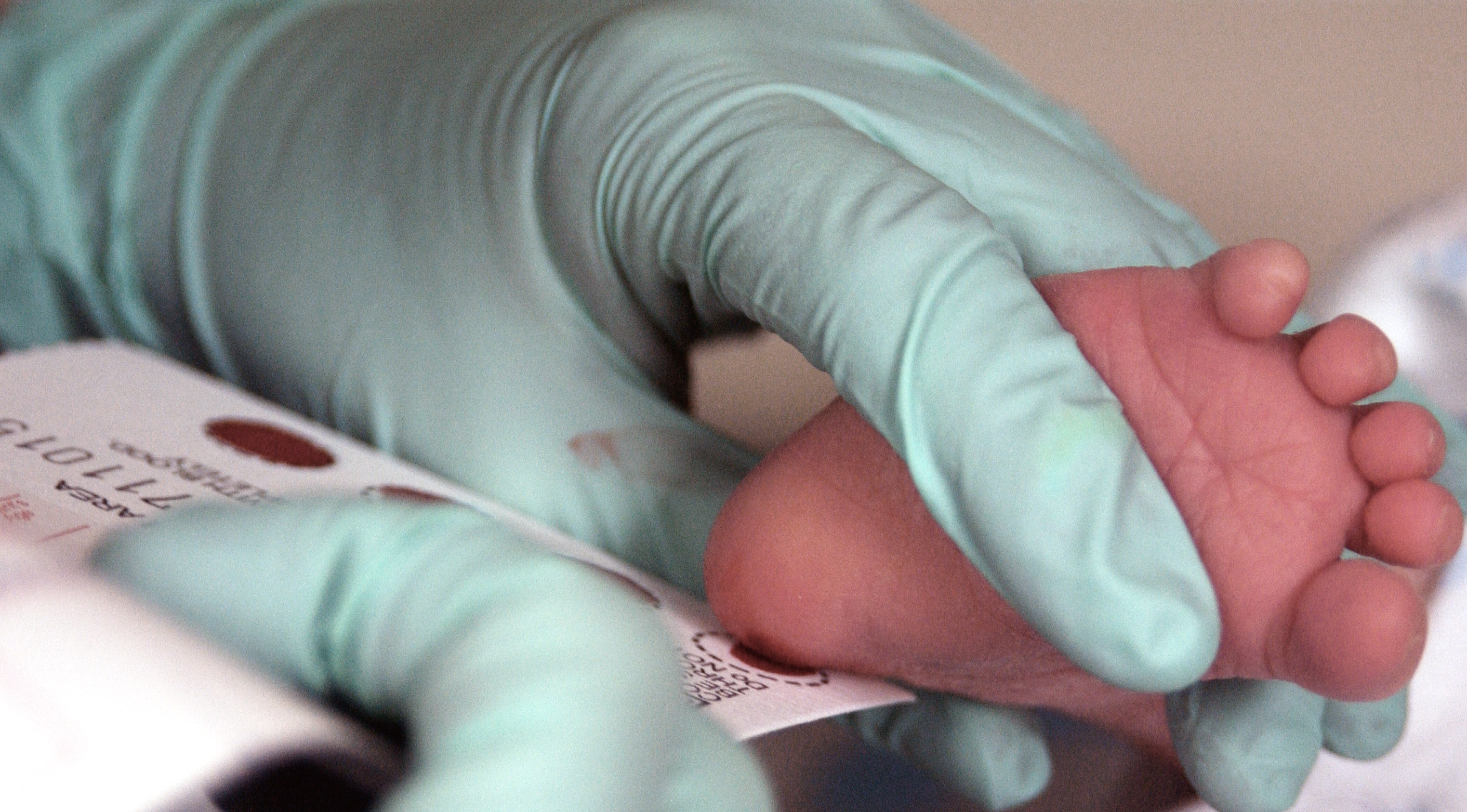 A nurse in a hospital nursery gently holding a newborn’s foot and collecting a few drops of blood on a screening card, real-life documentary photo style