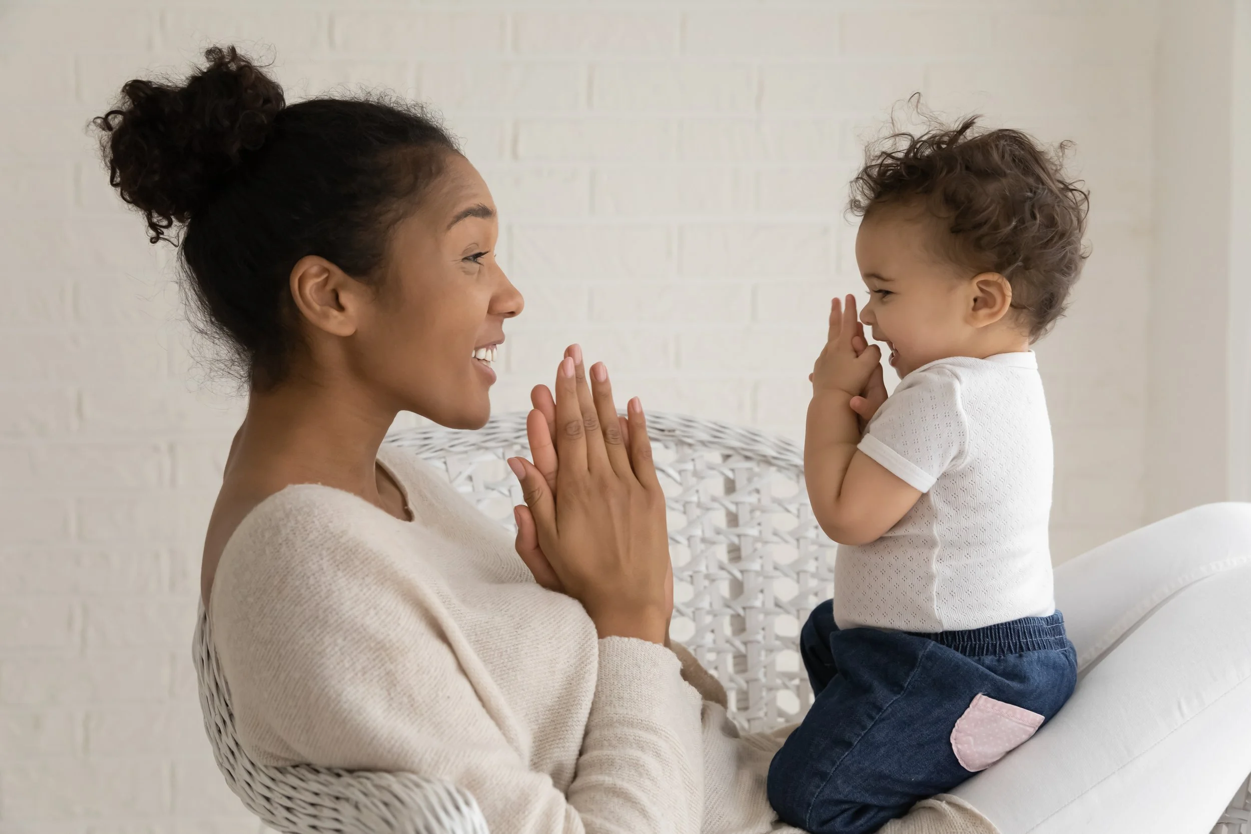 A parent and baby sitting together, both clapping and looking at each other