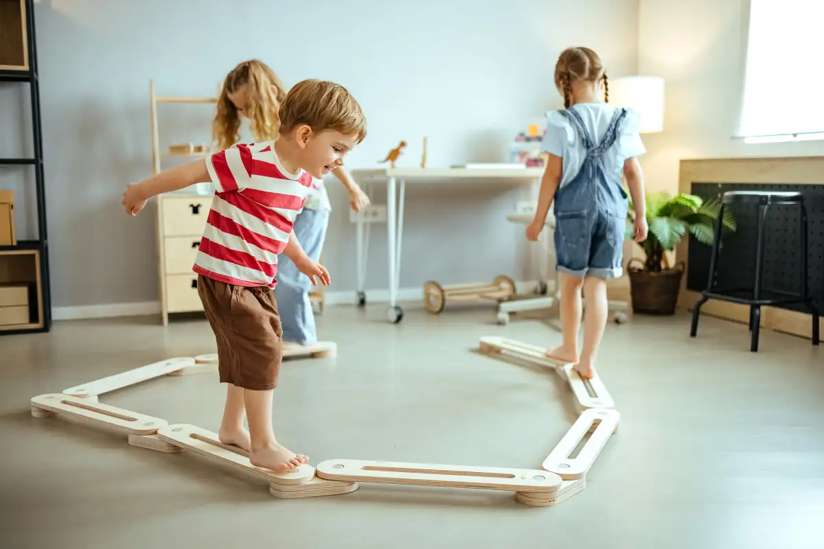 A parent and toddler playing a walking game in a hallway, with the toddler trying to walk with heels down while the parent demonstrates, candid indoor photo