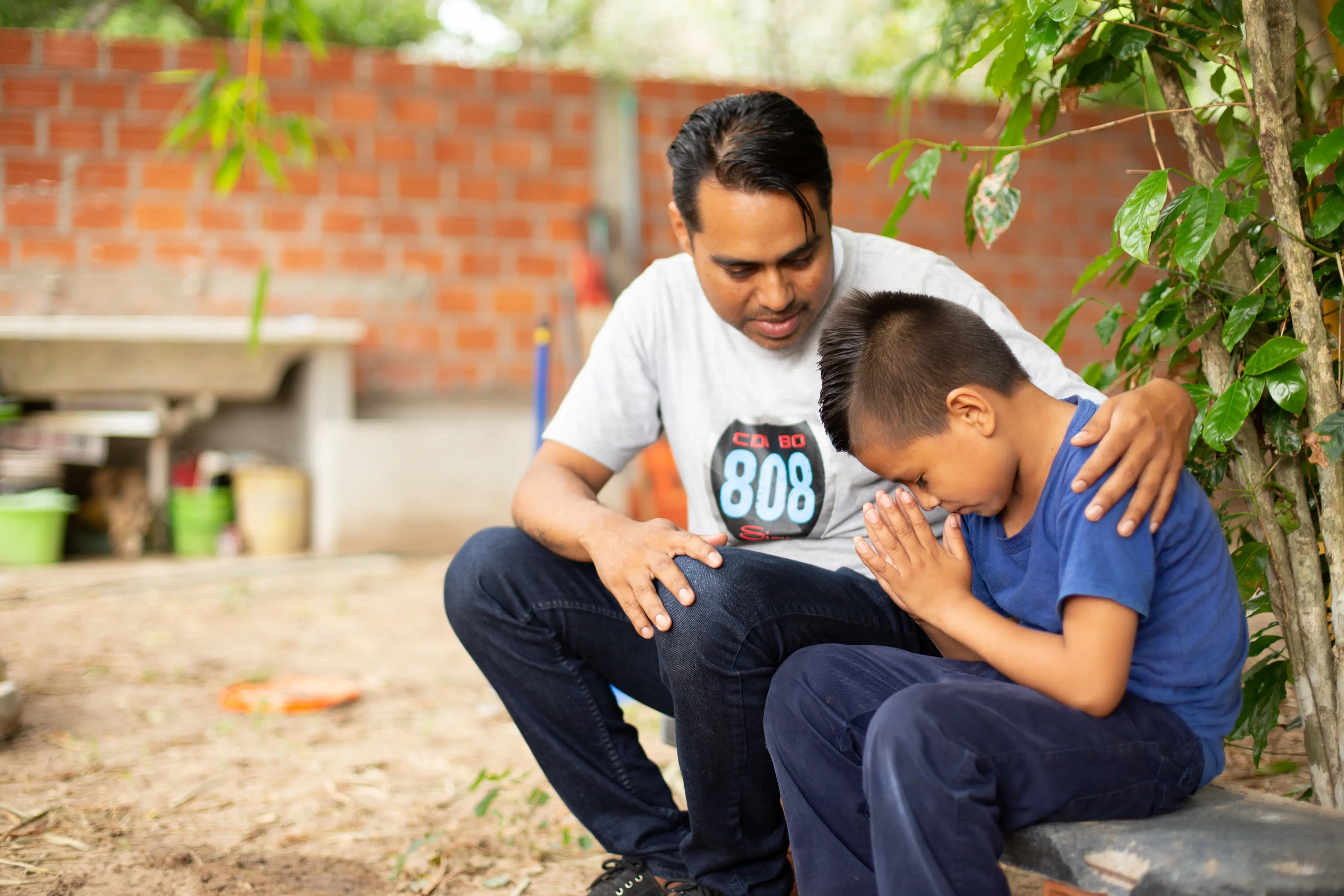 A parent and young child sitting on a shaded bench at an amusement park with the child sipping water and resting, candid photo