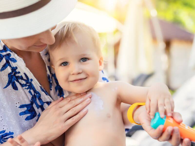 A parent applying a small amount of fragrance-free lotion to a toddler's mildly red forearm near a window with natural light, realistic photograph