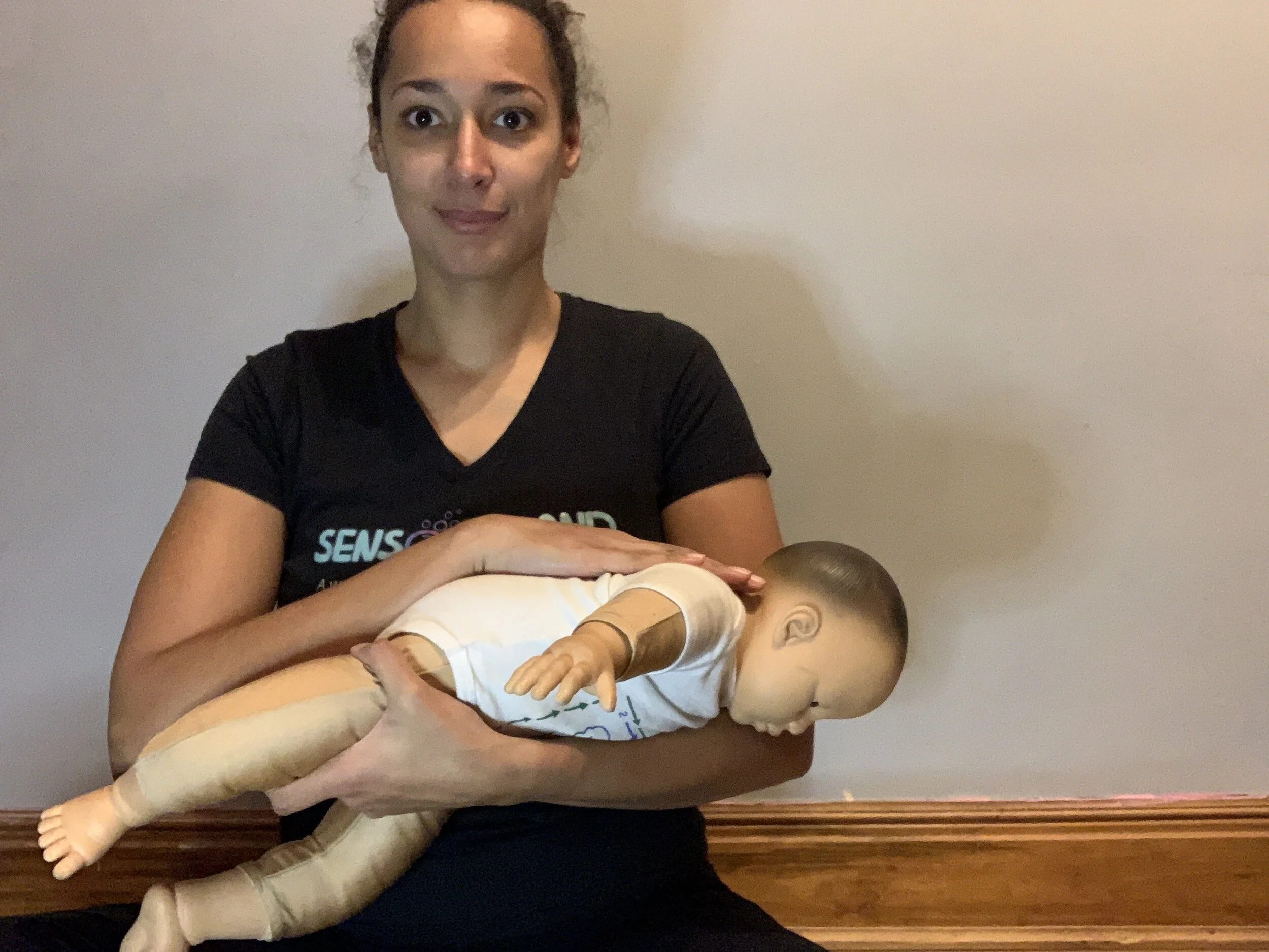 A parent gently bringing a newborn's knees toward their tummy on a changing pad, hands supporting the baby's legs in a careful, comforting position