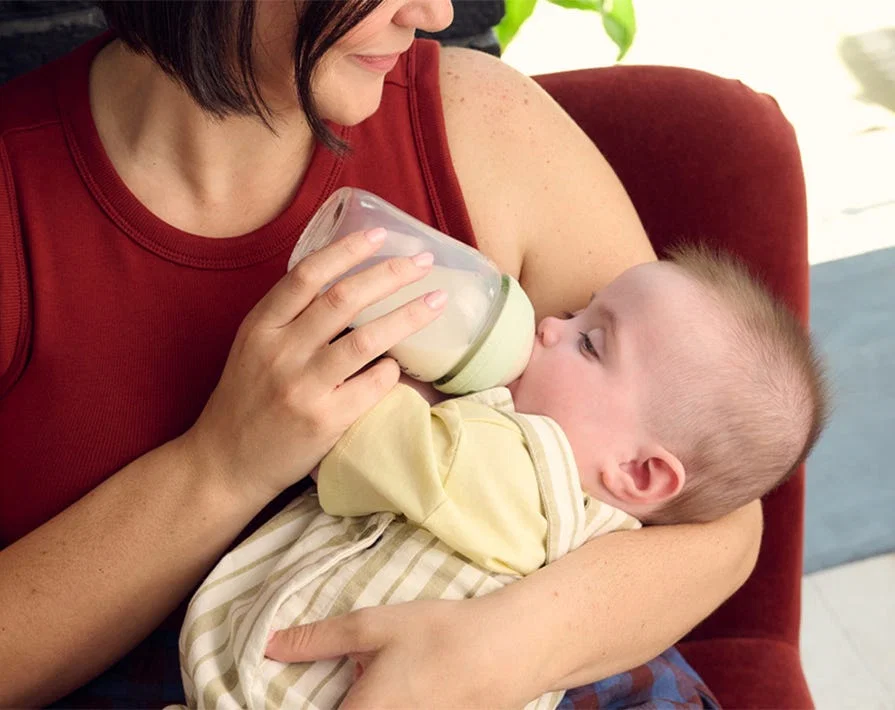 A parent gently burping a baby over their shoulder after a bottle feed, baby upright with a burp cloth, real photograph