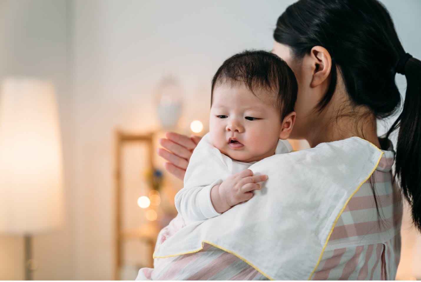 A parent gently burping a newborn over their shoulder in a softly lit living room, candid realistic photo