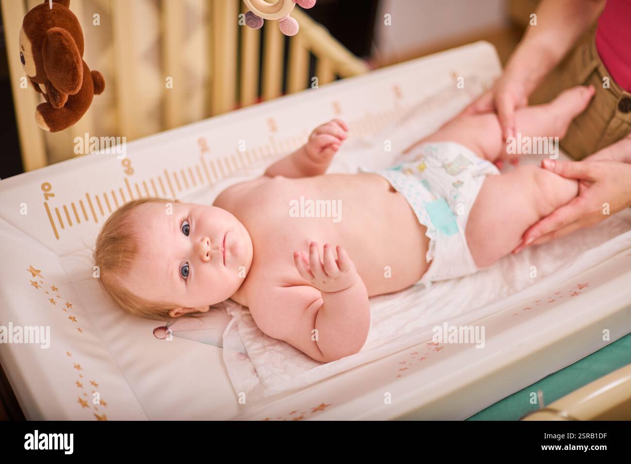 A parent gently changing a baby on a changing table with a diaper and ointment nearby, soft daylight, non-graphic