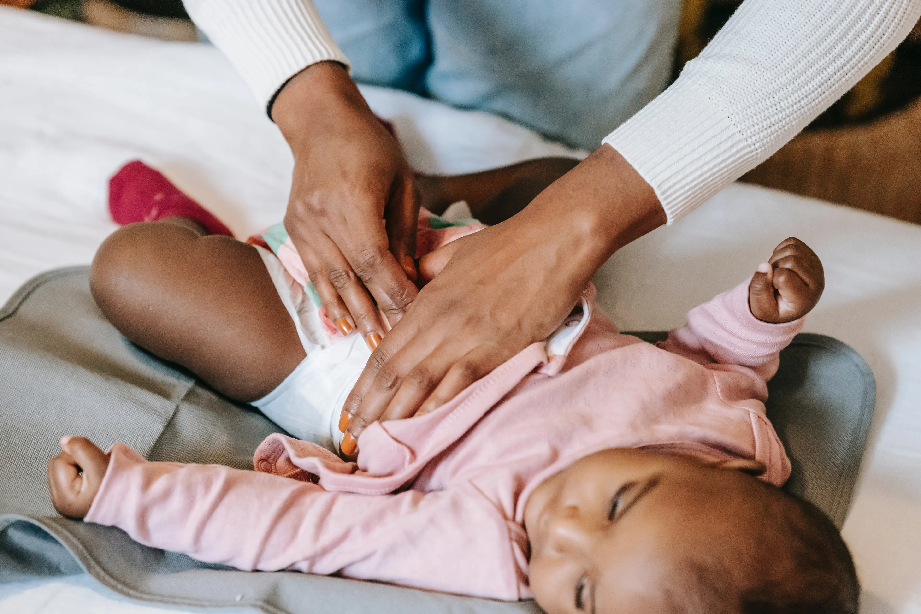 A parent gently changing a baby’s diaper on a changing table while applying barrier cream, warm home lighting, real-life photo style