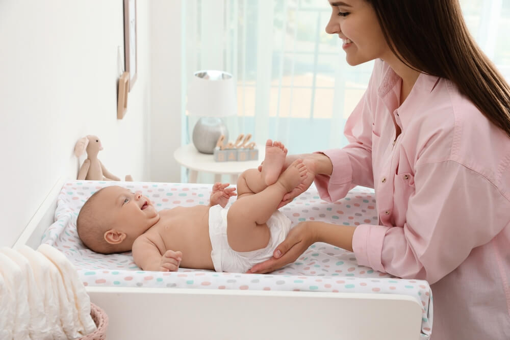 A parent gently changing a baby’s diaper on a changing table in a nursery with soft natural light, realistic photo