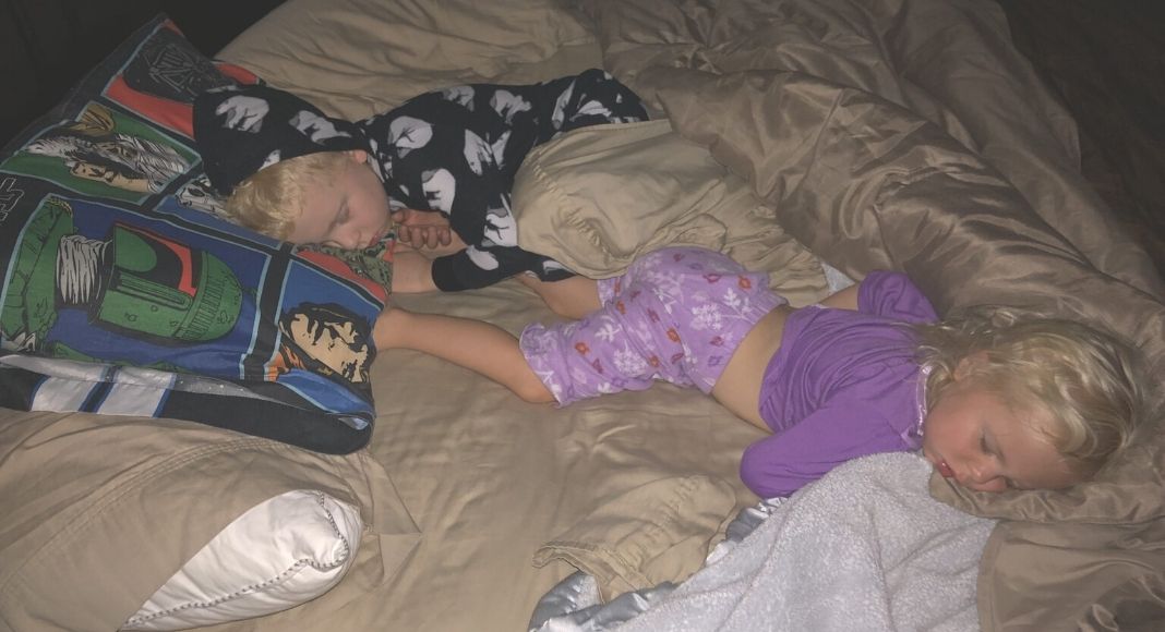 A parent gently holding a toddler's hand and guiding them back toward a bedroom doorway at night, softly lit home scene