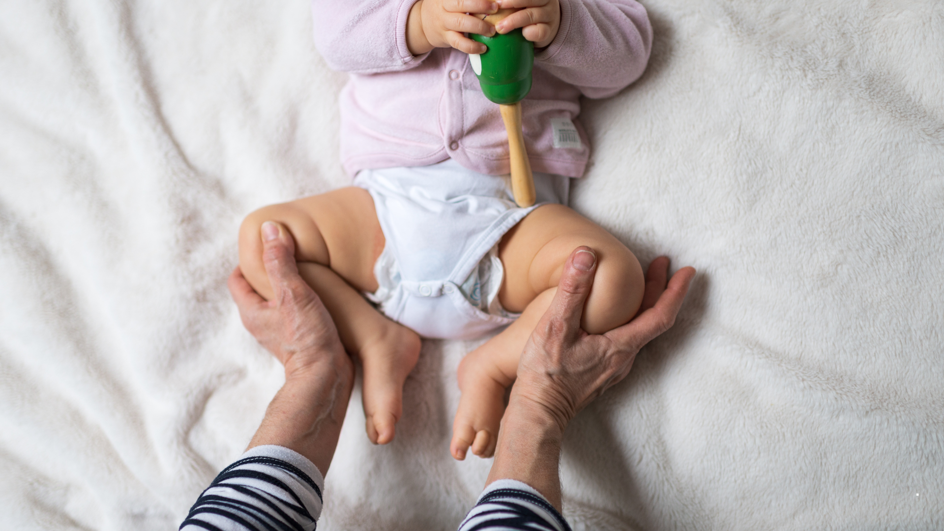 A parent gently lifting a baby's legs during a diaper change while looking closely at the baby's thigh creases in soft natural light, realistic photo