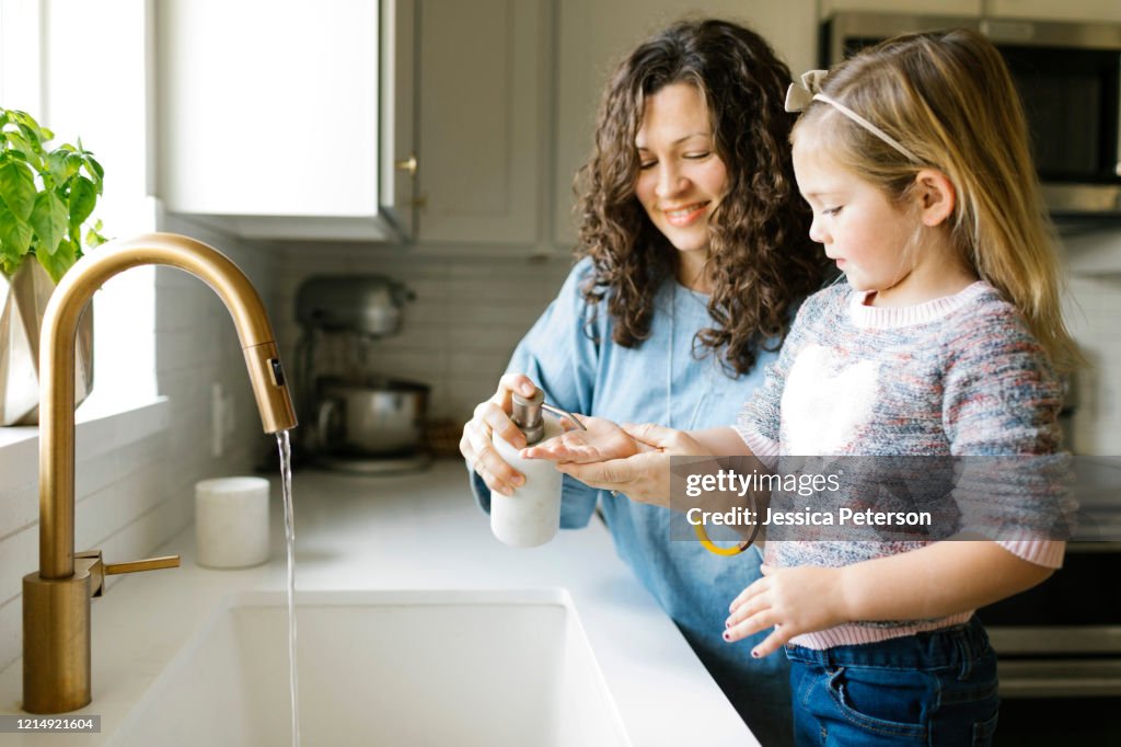 A parent gently rinsing a toddler's hands under lukewarm running water at a kitchen sink, realistic home photo