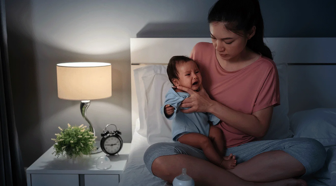 A parent gently soothing a baby back to sleep at night in a dark bedroom with a small night light