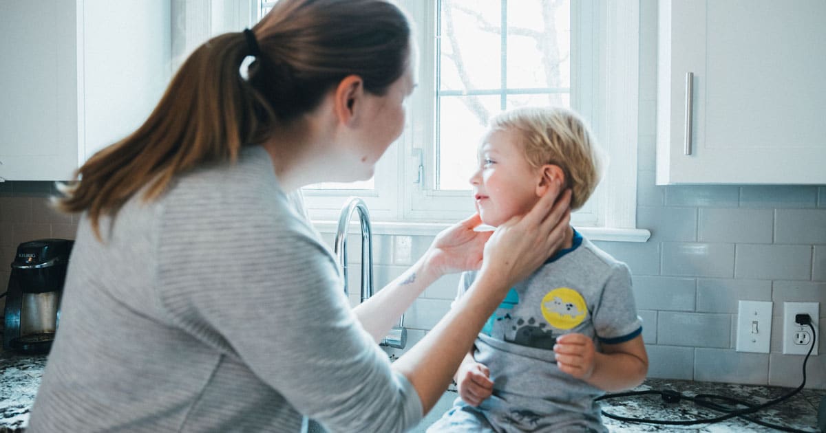 A parent gently wiping the outside of a toddler's ear with a soft damp washcloth in a bright bathroom, natural candid photo
