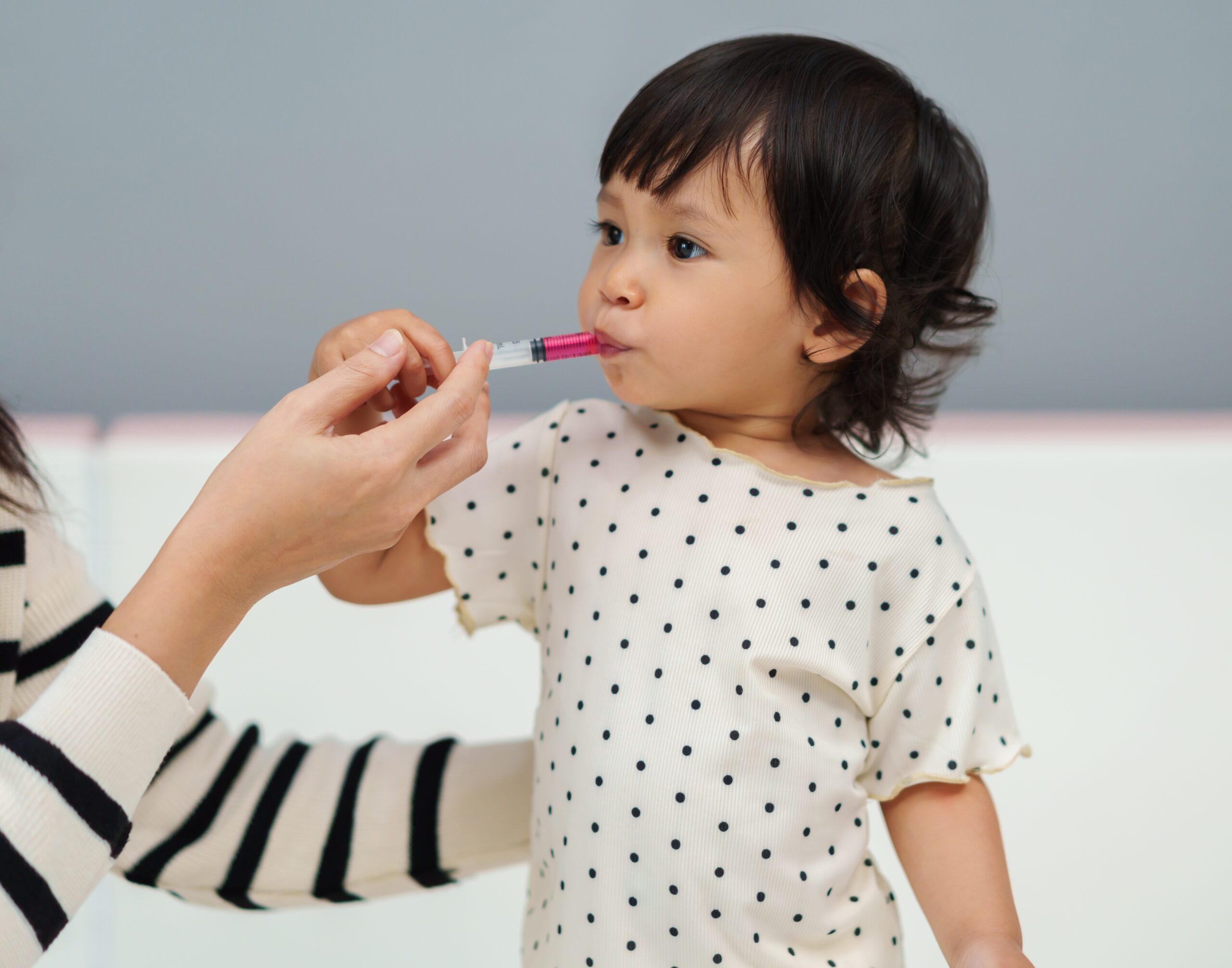 A parent giving a toddler liquid medicine with an oral syringe in a bright kitchen, candid realistic photo
