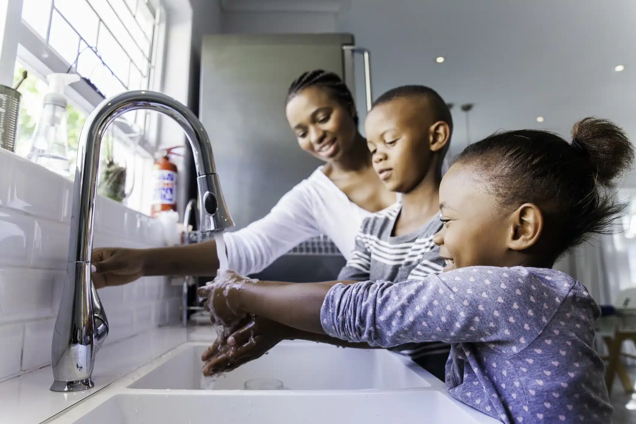 A parent helping a young child wash hands with soap at a kitchen sink, realistic photo