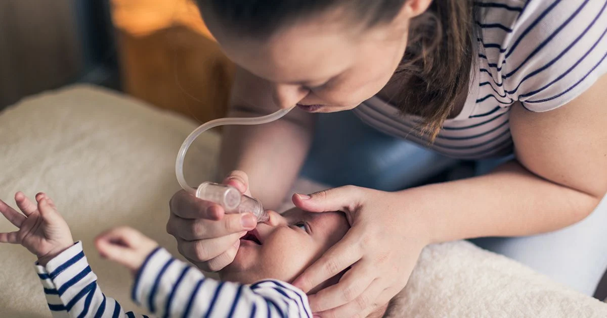 A parent holding a nasal suction device near a baby’s nose while gently steadying the baby’s head