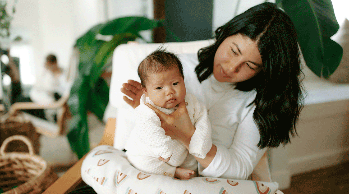 A parent holding a newborn upright against their shoulder while gently patting the baby's back after breastfeeding, cozy home setting, real photo style