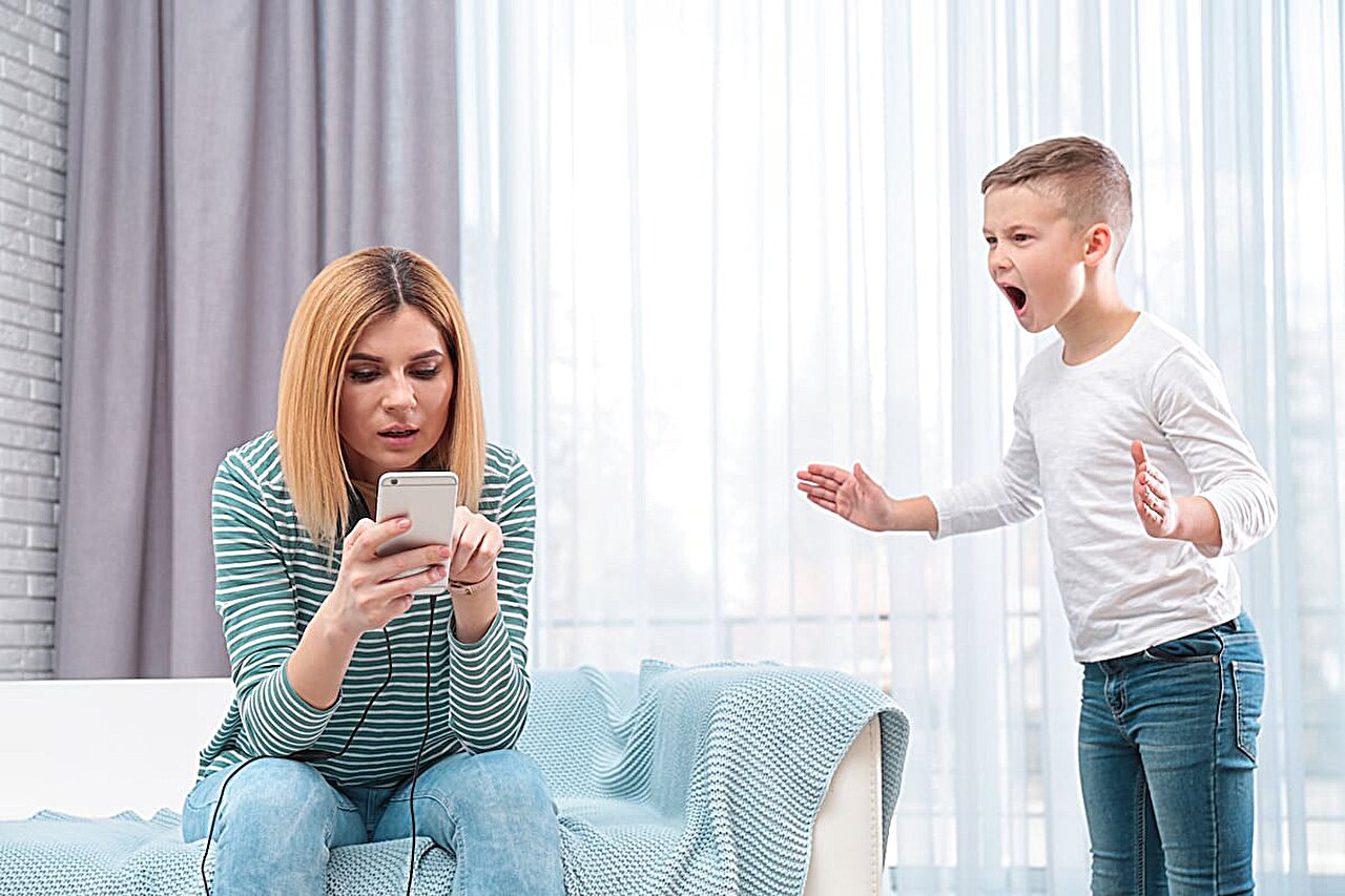 A parent holding a smartphone with a running timer while watching a toddler lying safely on their side on a rug, realistic home photo