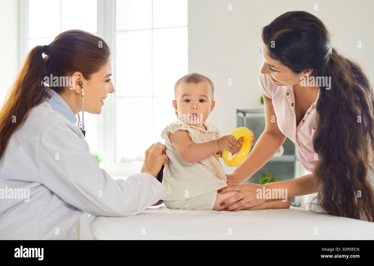 A parent holding a toddler in a pediatric clinic exam room while a clinician listens to the child’s lungs with a stethoscope, natural clinical photo