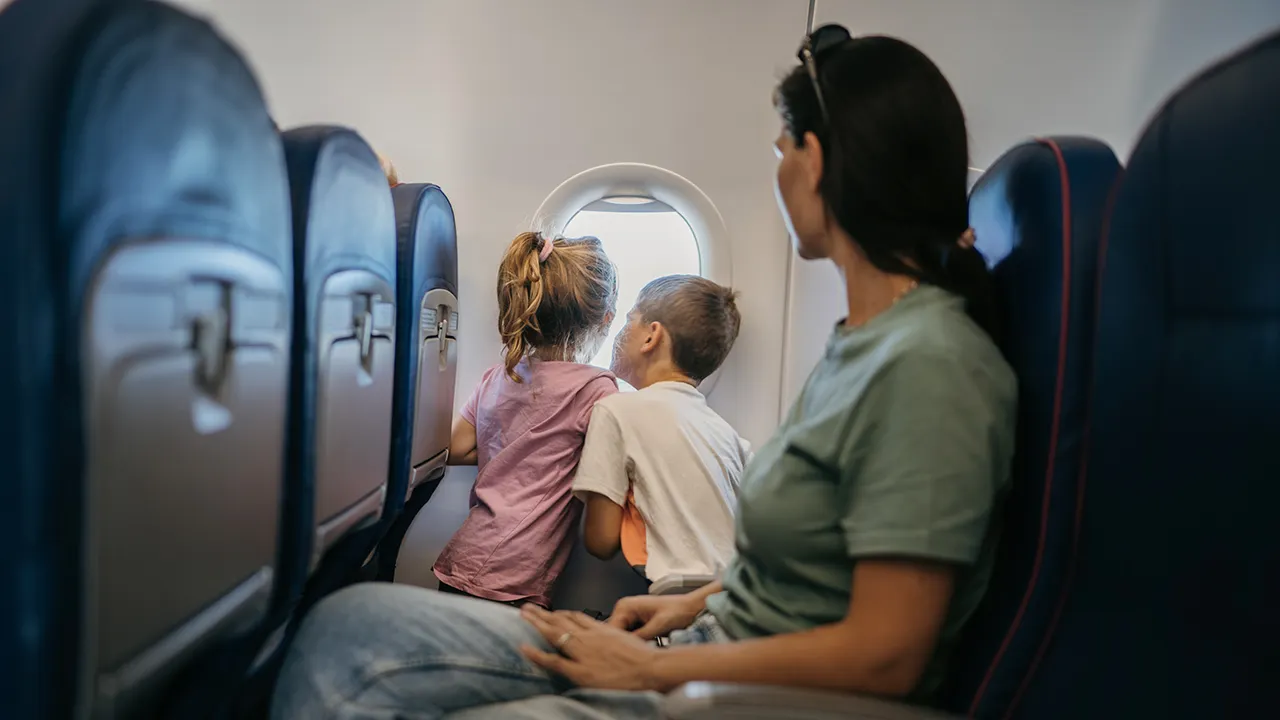 A parent holding a toddler on their lap in an airplane seat while the toddler looks out the window during daytime flight, natural travel photography
