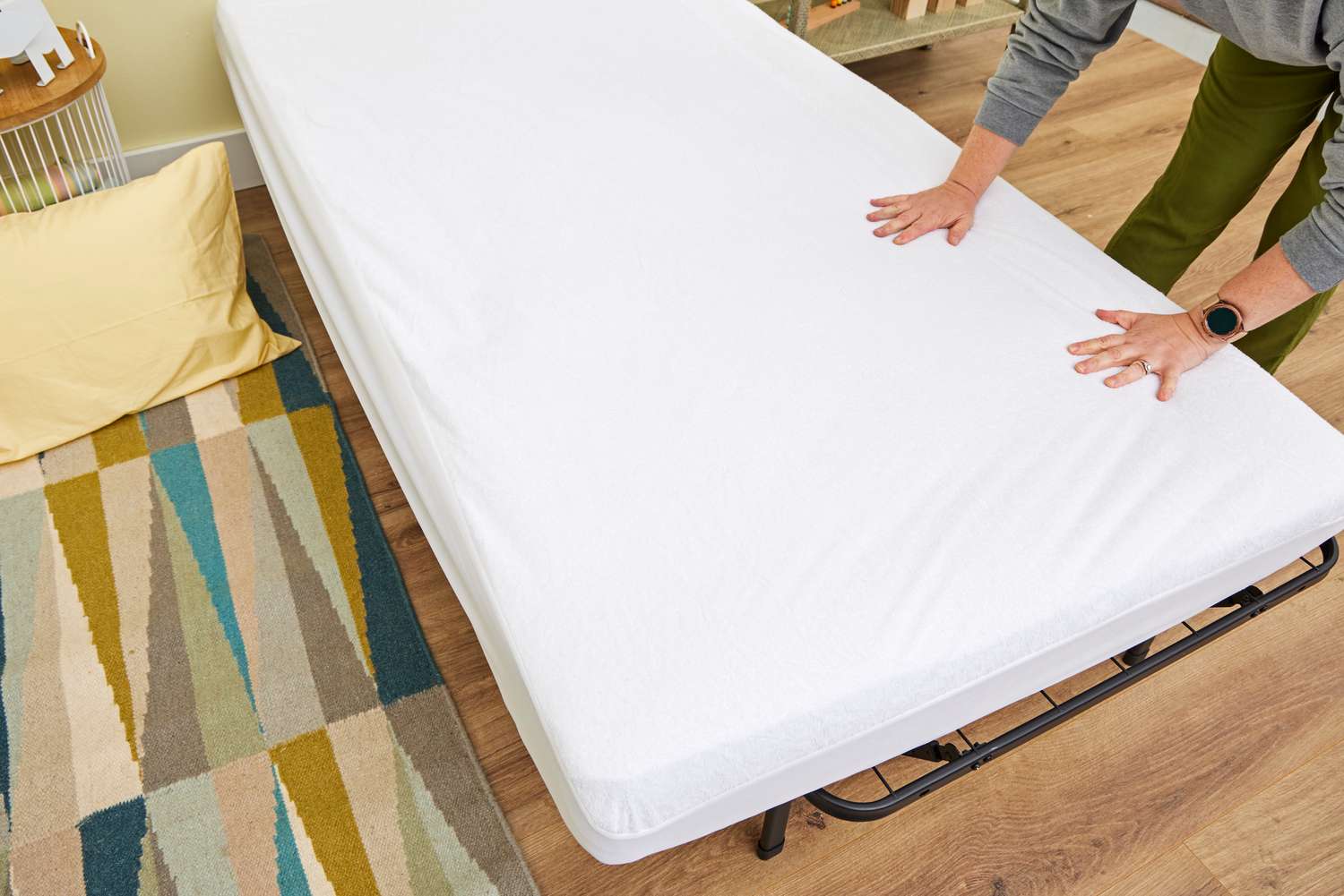 A parent pulling a clean white fitted sheet over a mattress that has a zippered allergy encasement underneath in a child’s bedroom, realistic home photo