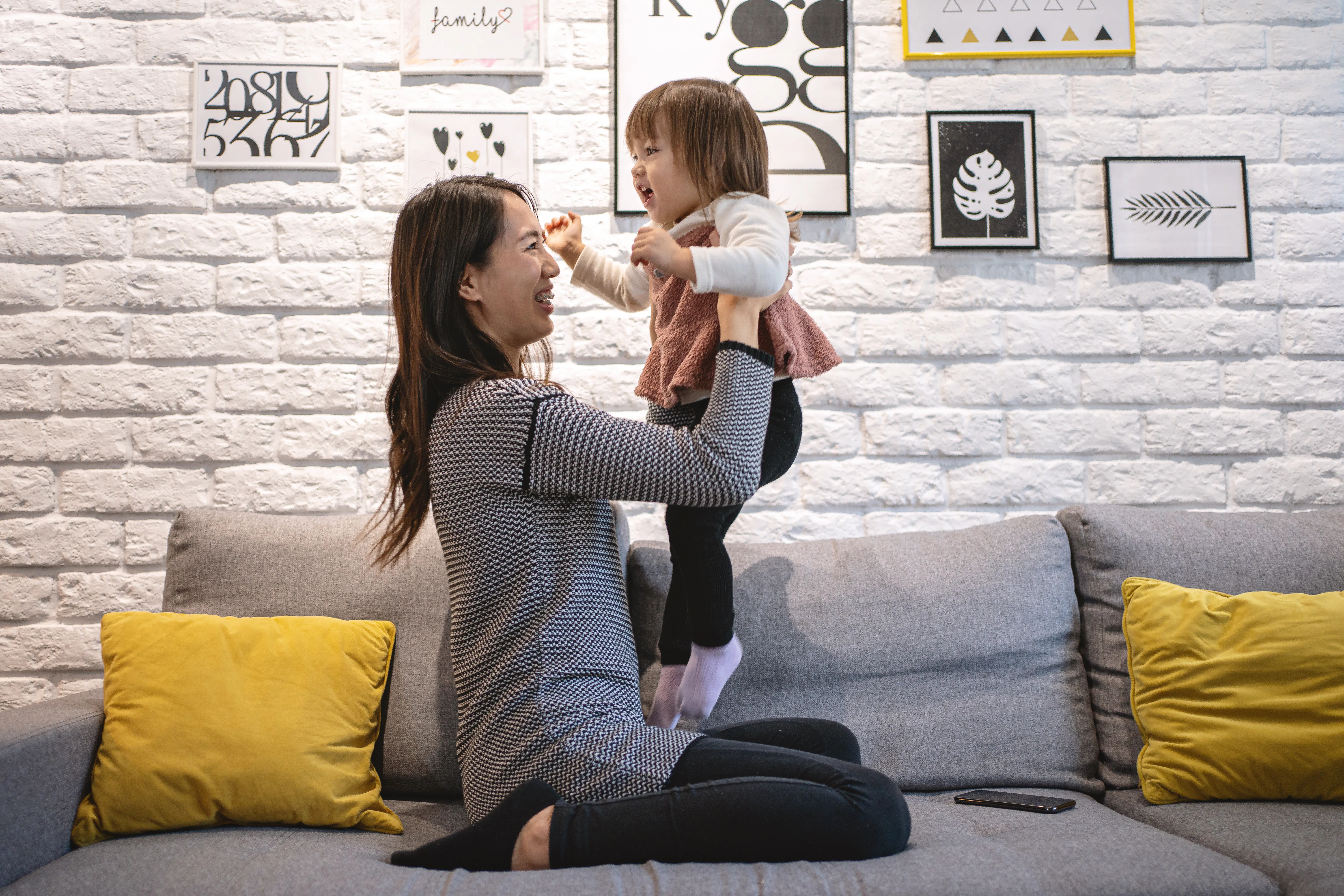 A parent safely lifting a toddler under the armpits in a bright living room, showing supportive hands and the child’s arms relaxed, realistic photo