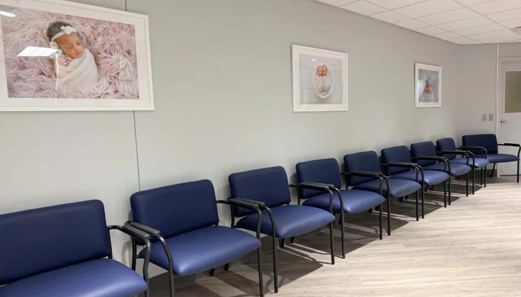 A parent sitting in a hospital radiology waiting area holding a baby wrapped in a blanket, documentary-style real photograph