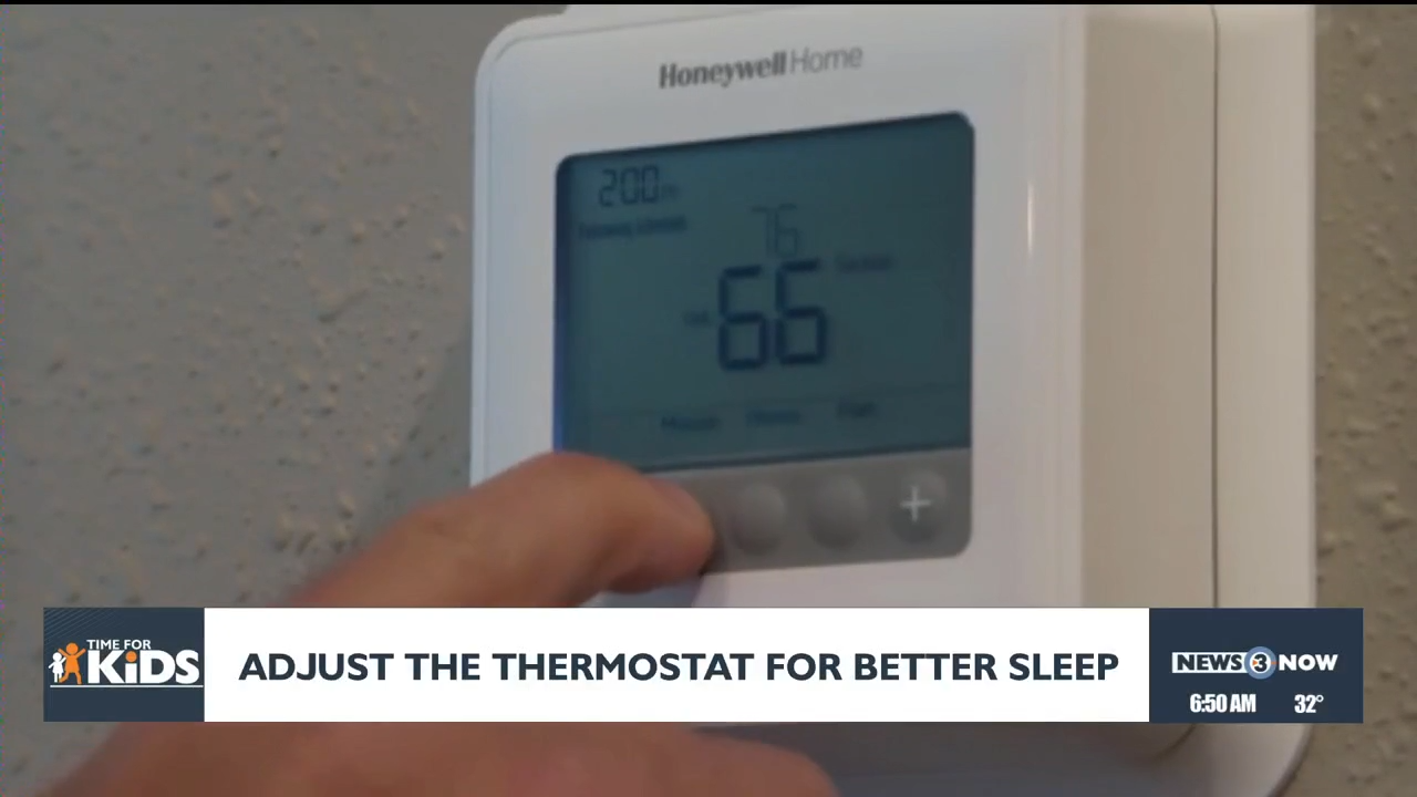 A parent’s hand adjusting a digital thermostat on a wall in a hallway near a child’s bedroom at night, realistic photo