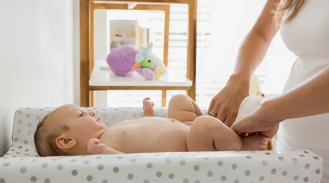 A parent’s hands gently changing a baby’s diaper on a changing table with a clean diaper and wipes nearby, warm home lighting, candid lifestyle photograph
