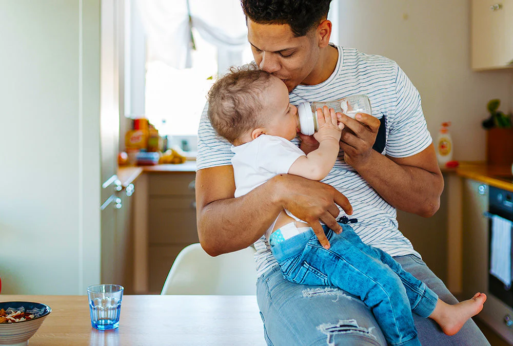 A parent’s hands holding a small bottle labeled as infant vitamin D supplement next to a baby’s changing table in a softly lit nursery, real photo