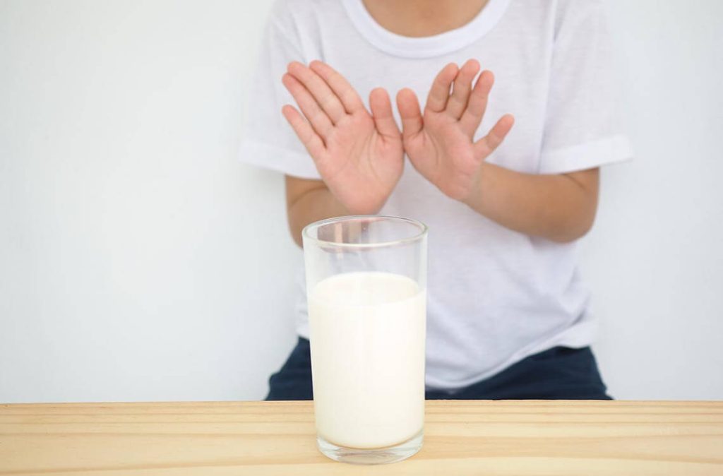 A parent’s hands pouring lactose-free milk from a carton into a small toddler cup on a kitchen counter, natural window light photo
